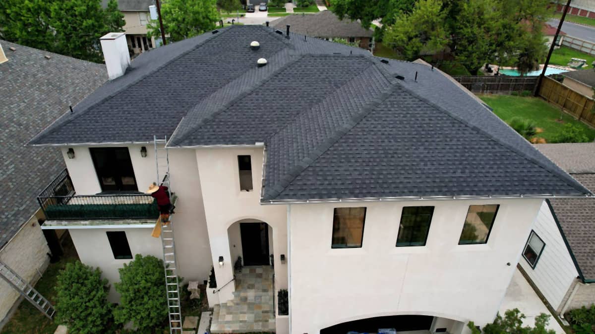 Aerial oblique view of a completed charcoal shingle roof on a white stucco two-story home in Bellaire, TX