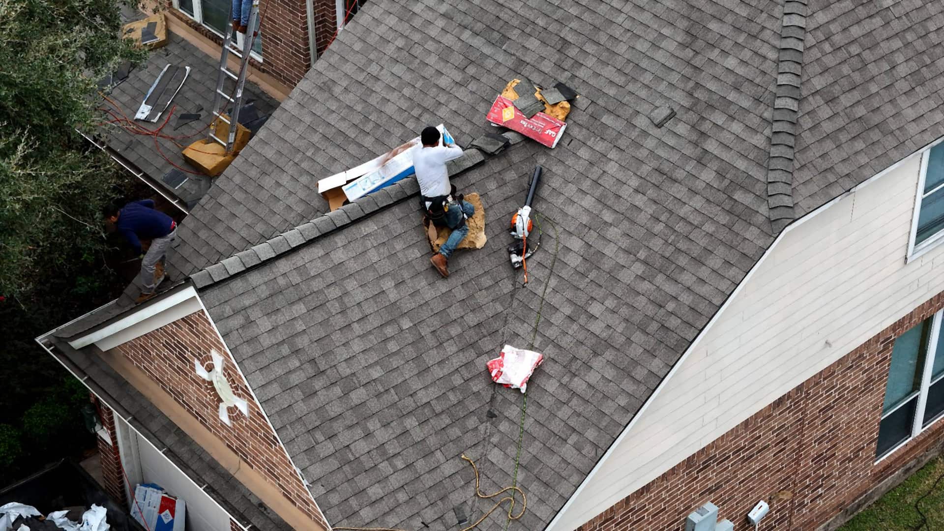 Close aerial of a roofer working a single section of a gray shingle roof on a Champions-area Houston home