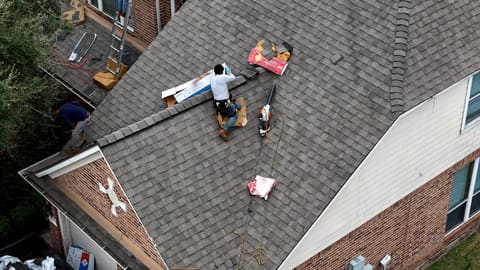 Close aerial of a roofer working a single section of a gray shingle roof on a Champions-area Houston home