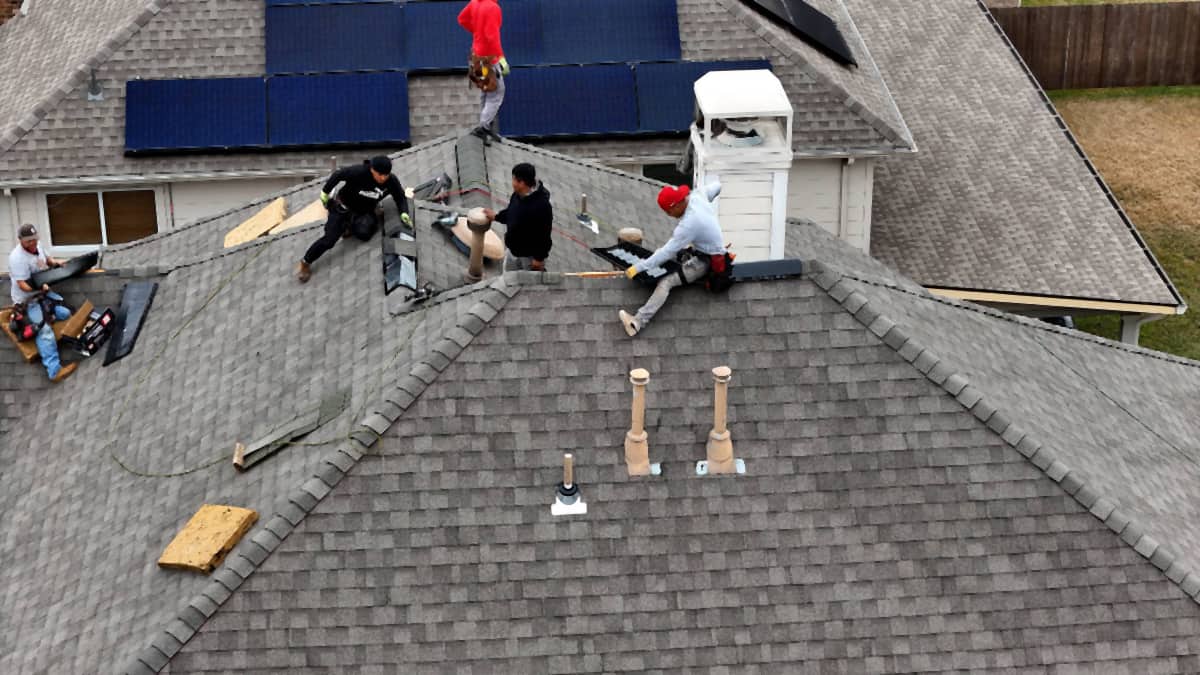 Handy Hands crew working along the ridge of a Champions-area Houston roof, with solar panels on the far slope