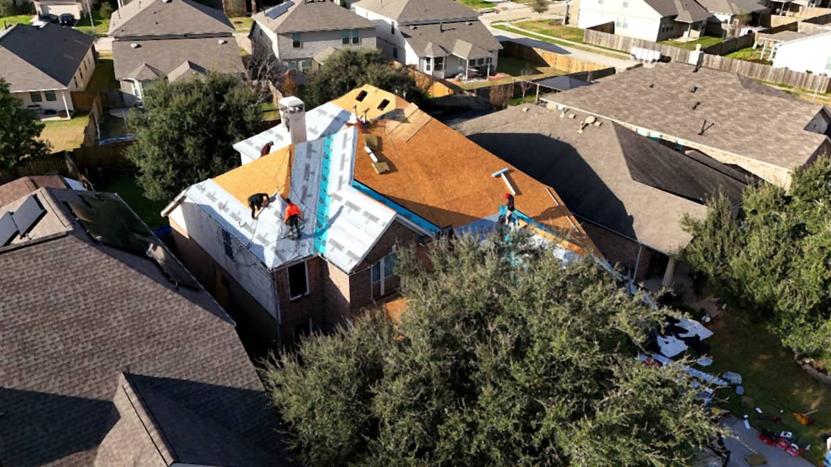 Aerial view of a Champions-area Houston roof stripped to bare decking during tear-off, with waterproofing already run where the roof meets the walls
