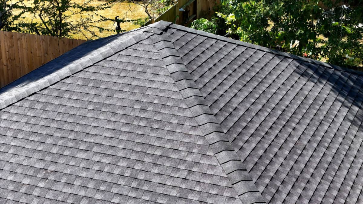 Close aerial view of finished shingle courses and hip caps meeting at the peak of a Cypress, TX roof