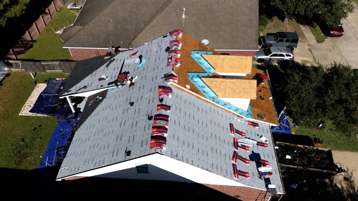 Top-down aerial of a Cypress, TX roof dried in with synthetic underlayment, shingle bundles staged across the slopes