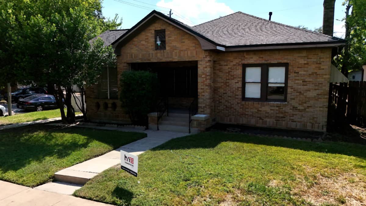 Front view of a Riverside, Houston brick bungalow with a completed shingle roof replacement and a Handy Hands yard sign in the lawn