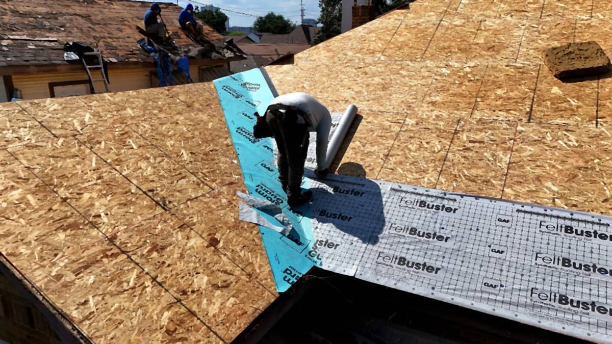 Roofer rolling GAF FeltBuster synthetic underlayment across a Riverside, Houston roof deck, with self-adhered membrane in the valley