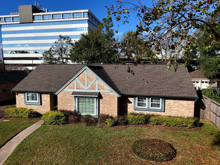 Front elevation of a brick Spring Branch, Houston home with a completed brown shingle roof replacement