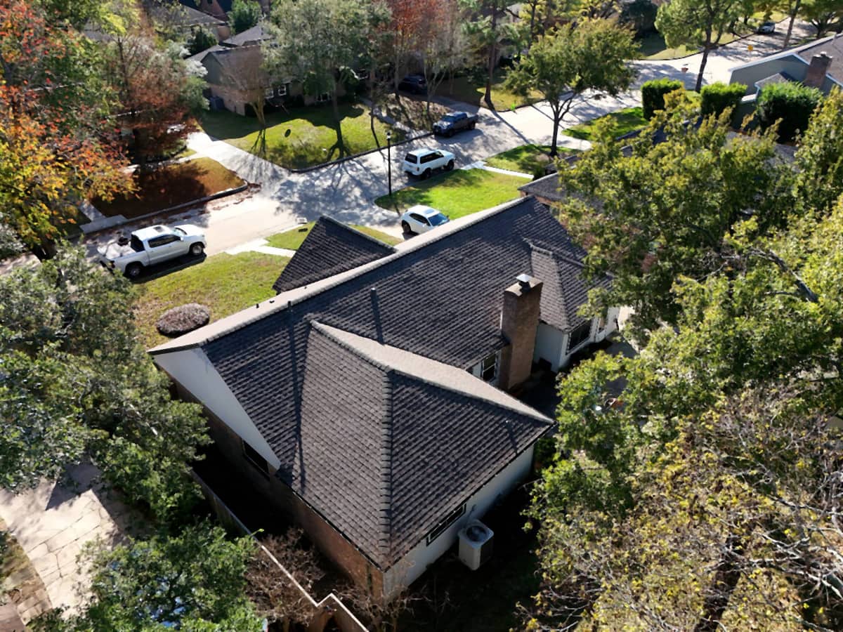 High aerial view of a completed dark shingle roof replacement on a Spring Branch, Houston home, seen from above the street