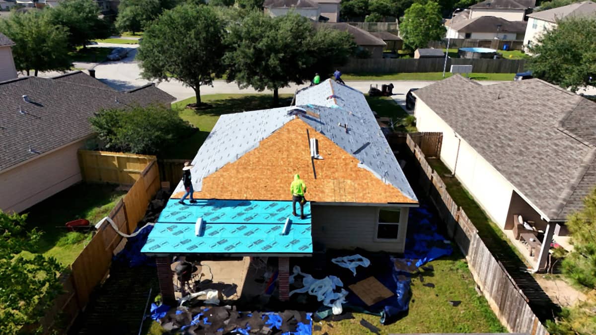 Crew rolling synthetic underlayment across a Spring, TX roof deck, with self-adhered membrane covering the low-slope porch below