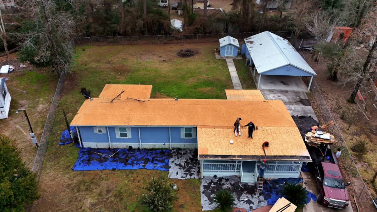 Aerial view of a Spring, TX home stripped to bare roof decking, with old shingles piled on tarps in the yard