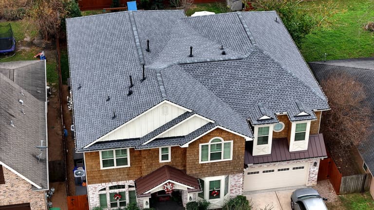 Aerial view of a completed gray shingle roof replacement on a two-story Timbergrove home in Houston