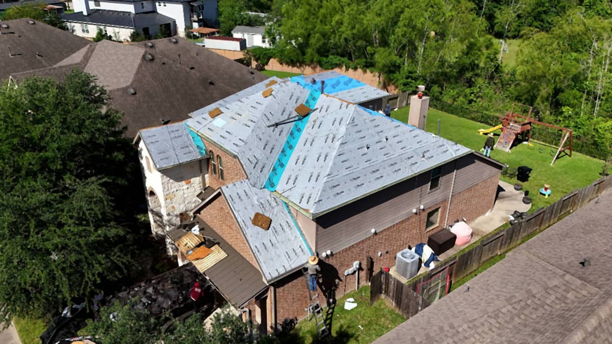 Aerial view of a large Tomball, TX roof dried in with synthetic underlayment, with self-adhered membrane in the valleys and around the chimney