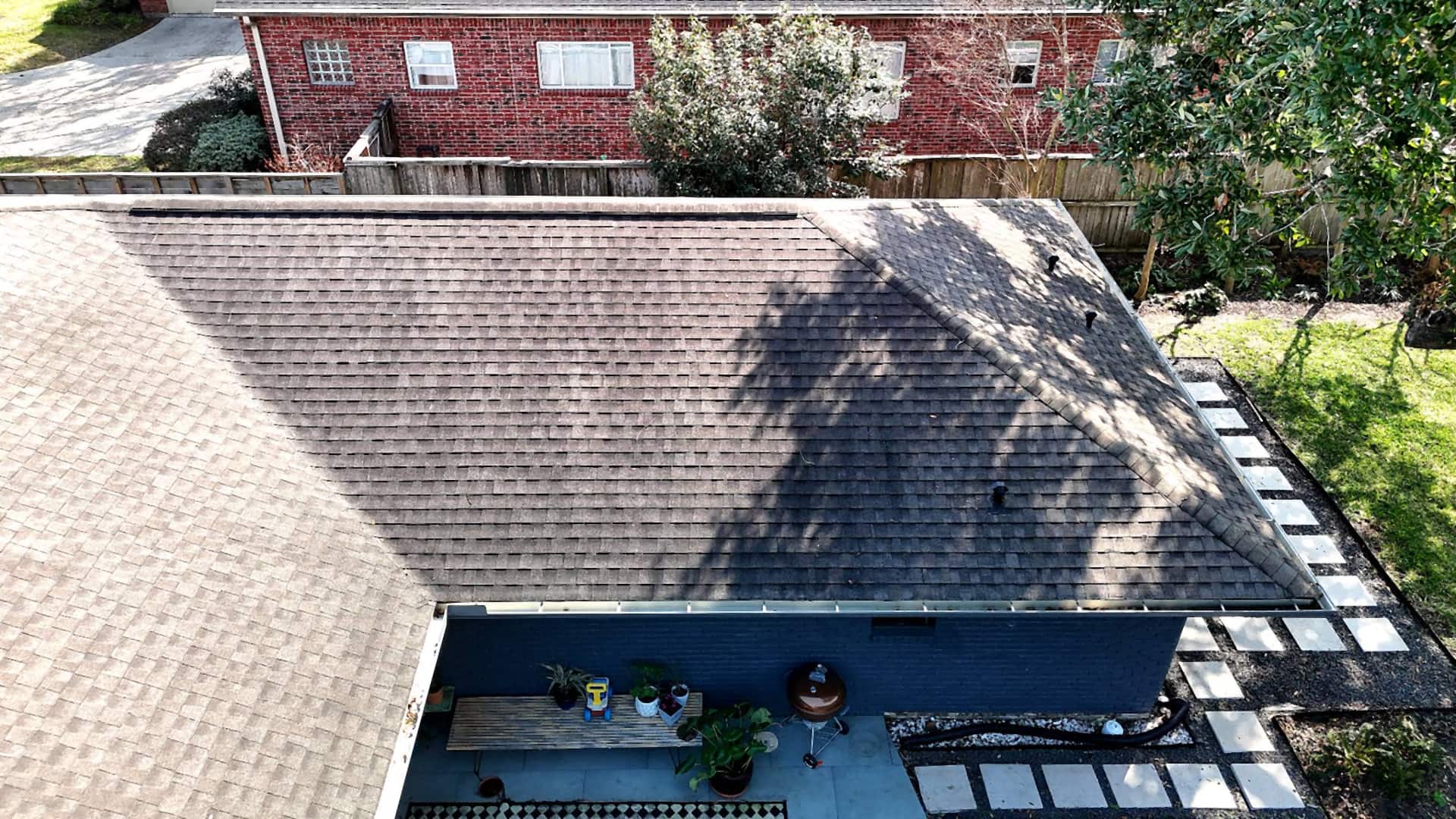 Overhead view of a completed brown shingle roof and new drip edge above a back patio on a Westbury, Houston home
